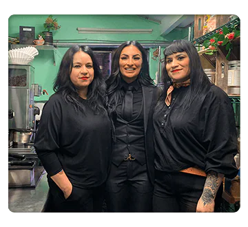 Square shaped photo of three women in all black standing in a restaurant kitchen setting